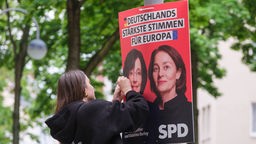Frau hängt Wahlplakate der SPD für die Europawahl 2024 mit den Portraits von Olaf Scholz und Katarina Barley auf, Köln, 26.04.2024.