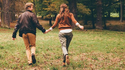 Ein Mann und eine Frau laufen Hand in Hand durch einen Wald.
