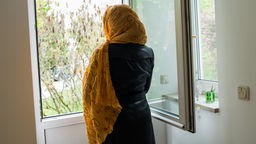 Symbolbild: Eine in ihr Kopftuch eingehüllte Muslima steht an einem geöffneten Fenster.