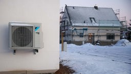 Eine Luftwärmepumpe ist bei Schnee und Eis an einer Hauswand in einem Einfamilienhausgebiet zu sehen.
