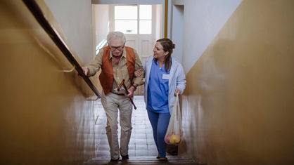 Lächelnde Pflegerin hilft einem Senior beim Treppensteigen.