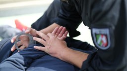 Symbolbild: Eine NRW-Polizeikraft legt einer Person Handschellen an.