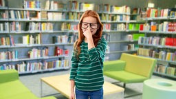 Mädchen mit großer Brille steht in einer Bücherei