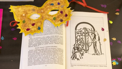 Eine Maske und Konfetti liegt auf Buch Ester, aus dem zu Purim traditionell vorgelesen wird liegt. Symbolbild