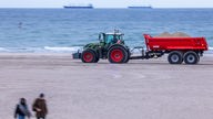 Ein Traktor transportiert Sand in einem Anhänger am Strand von Warnemünde. 