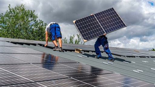 Symbolbild: Zwei Menschen decken ein Dach mit Solarmodulen
