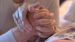 Zwei Hände halten die Hand einer Patientin im Bett