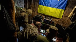 Ukrainische Soldaten sitzen vor Displays und steuern einen Drohnen-Einsatz. 