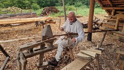 Ein Mann in mittelalterlicher Kleidung bearbeitet ein Holzstück.