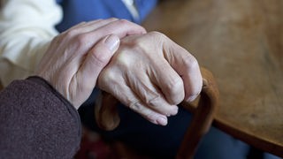 Ein Mensch hält die Hand eines älteren Menschen.