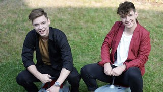 Die Zwillinge Heiko und Roman Lochmann, bekannt als "die Lochis": zwei junge Männer sitzen auf einer Wiese auf Spielzeugautos