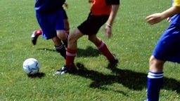 Archivbild: Ein Fußball und Beine von Jugendlichen auf einem Fußballfeld