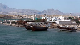 Vor der kleinen Stadt Sur im Oman liegen Dau-Schiffe in einer Werft, im Hintergrund Berge