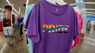 In einem Geschäft hänggt ein lilafarbenes t-Shirt mit dem regenbogenfarbenen Aufdruck "Pride".