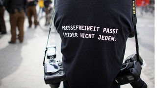 Ein Fotograf trägt am Rande einer Demonstration ein T-Shirt mit einem Slogan für die Pressefreiheit.
