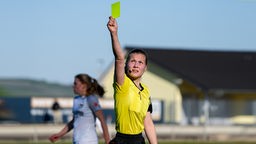 Eine junge Schiedsrichterin zeigt die gelbe Karte.