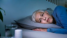 Eine Frau liegt im Bett und schaut besorgt auf ihren Wecker
