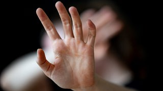 Eine Hand wird mit verkrümmten Fingern, wie aus Angst, zum Schutz erhoben.