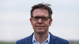 Porträt von Stefan Mau mit schwarzer Brille und blauem Sakko.