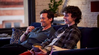 Hugh Jackman und Zen McGrath sitzen in ihren Rollen in "The Son" auf einem Sofa und schauen vermutlich Fernsehen.