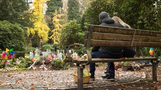 Zwei Menschen sitzen auf einer Bank auf einem Friedhof