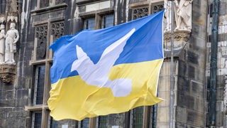 Vor einer Fassade hängt eine ukrainische Flagge mit einer Friedenstaube.