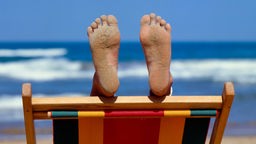 Symbolbild Langeweile im Urlaub: Zwei Füße ragen aus einem Liegestohl hervor.