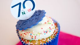 Ein Cupcake mit einer Verzierung, auf der zu lesen ist: "70 Jahre NRW" 
