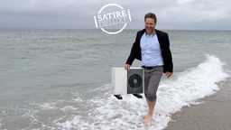 Satirische Bildmontage: Robert Habeck am Strand hält eine Wärmepumpe 