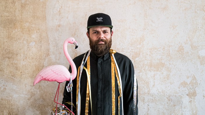 Patrick Salmen steht vor einer verwaschenen Wand und hat eine Flamingo-Figur in der Hand; Foto: Fabian Stuertz