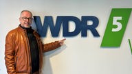 Robert Griess steht vor dem Logo von WDR5.