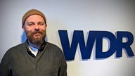 Patrick Salmen posiert vor dem WDR-Logo