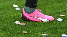 Schokotaler liegen bei einem Fußballbundesligaspiel auf dem Rasen, dazwischen der Fuß eines Fußballers
