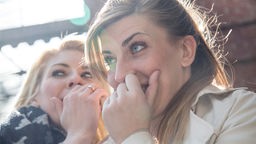 Zwei junge Frauen flüstern und lachen hinter vorgehaltener Hand.