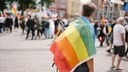 Symbolbild queere Gesellschaft: Ein Mann trägt eine Regenbogenfahne über der Schulter