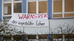 Ein Transparent mit der Aufschrift "Warnstreik der angestellten Lehrer" hängt am Gebäude einer Schule.