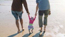 Rückansicht von zwei erwachsenen Menschen mit einem Kleinkind beim Strandspaziergang