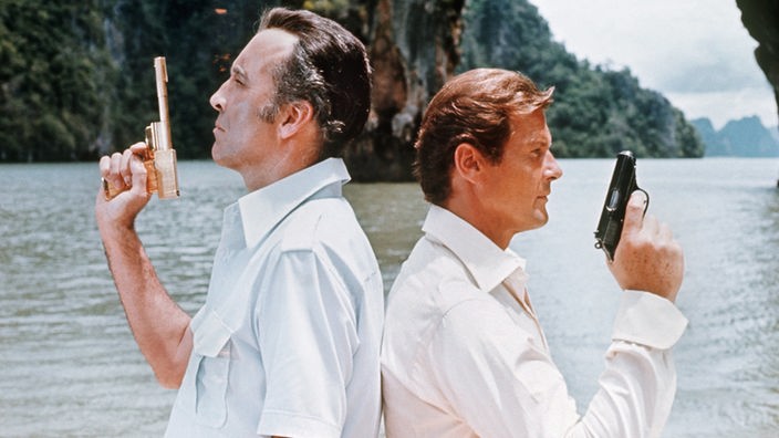 Christopher Lee und Roger Moore als "James Bond" stehen Rücken an Rücken mit einer Pistole in der Hand