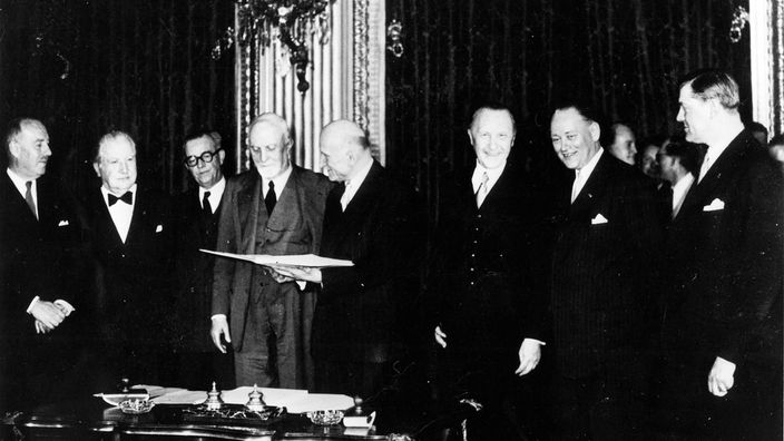 Schwarz-weiß-Foto: Bei der Unterzeichnung des Montanunion-Vertrages stehen acht Männer in dunklen Anzügen um einen Tisch, einer von ihnen hält den Vertrag in Händen