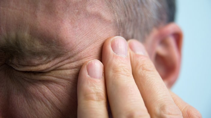 Mann hält sich schmerzverzerrt das Ohr