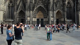 Touristen stehen vor dem Dom in Köln und machen Fotos