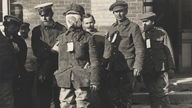 Ein englischer Kriegsgefangener mit einem Gesichtsverband nach einem Gasangriff in Flandern nach 1915, der von einem deutschen Soldaten abgeführt wird (Aufnahmedatum unbekannt)