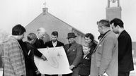 Lagerpfarrer Wilhelm Scheperjans (3.v.l.) zeigt Flüchtlingen aus Böseckendorf am 23.02.1963 im Lager Friedland den Bauplan für die geplante Neubausiedlung Neu-Böseckendorf