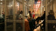 Besucher des Deutschen Auswanderer-Museums sitzen in nachgestellten Kulissen der US-Einwandererkontrolle von Ellis Island in New York
