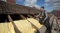 Eine Dachdeckerin verlegt Isoliermaterial auf dem Dach