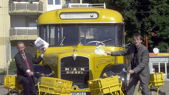 Gelber Postbus von 1946, davor 2 Männer in Anzügen auf gelben Postfahrrädern