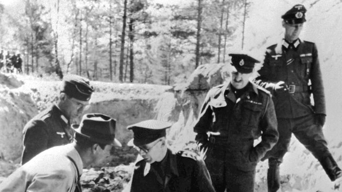 Bei der Besichtigung der Gräber von Katyn 1943: (v. l. n. r.) ein deutscher Offizier als Dometscher, ein Beamter des Propagandaministeriums (in Zivil), zwei kriegsgefangene Angehörigen der britischen Armee, Captain Gilder und Oberstleutnant Stevenson und ein mit Namen nicht geannter deutscher Offizier