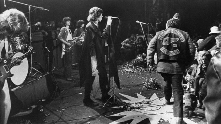 Mick Jagger am Mikro und heranstürmende Hells Angels auf der Bühne bei Rolling-Stones-Auftritt in Altamont
