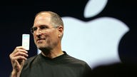 Steve Jobs hält einen iPod hoch, im Hintergrund das Apple-Logo