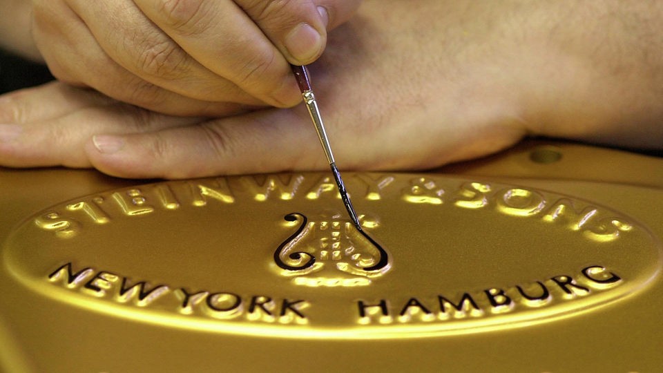 groß: Hand mit Pinsel, malt Steinwy-Signet auf goldene Gussplatte